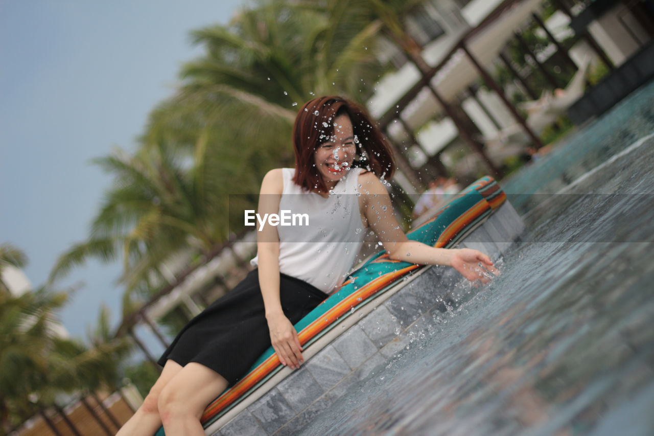 Cheerful woman splashing water while lying at poolside