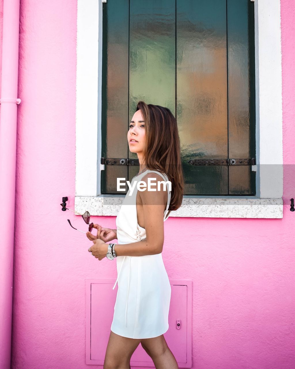 YOUNG WOMAN STANDING AGAINST PINK WINDOW