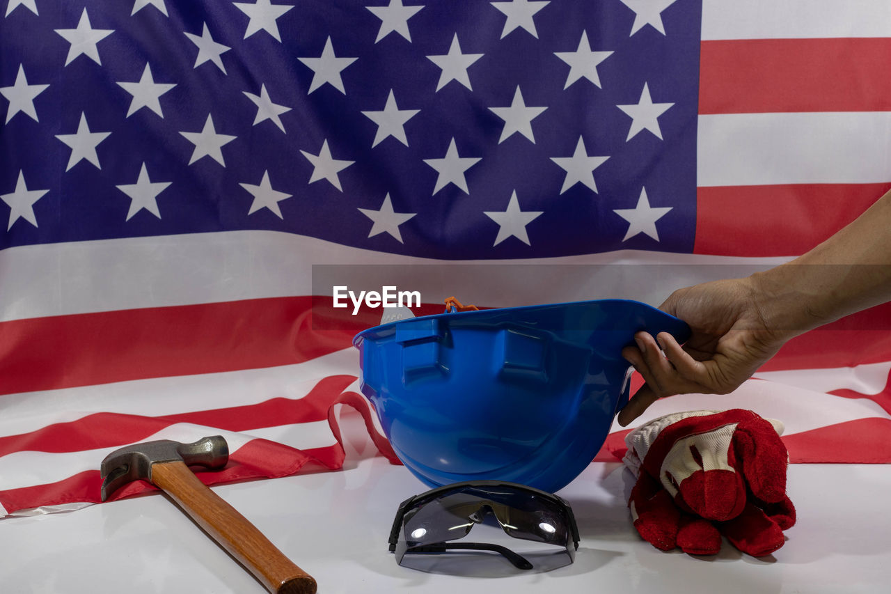 Cropped hand of person holding hardhat by work tools and american flag