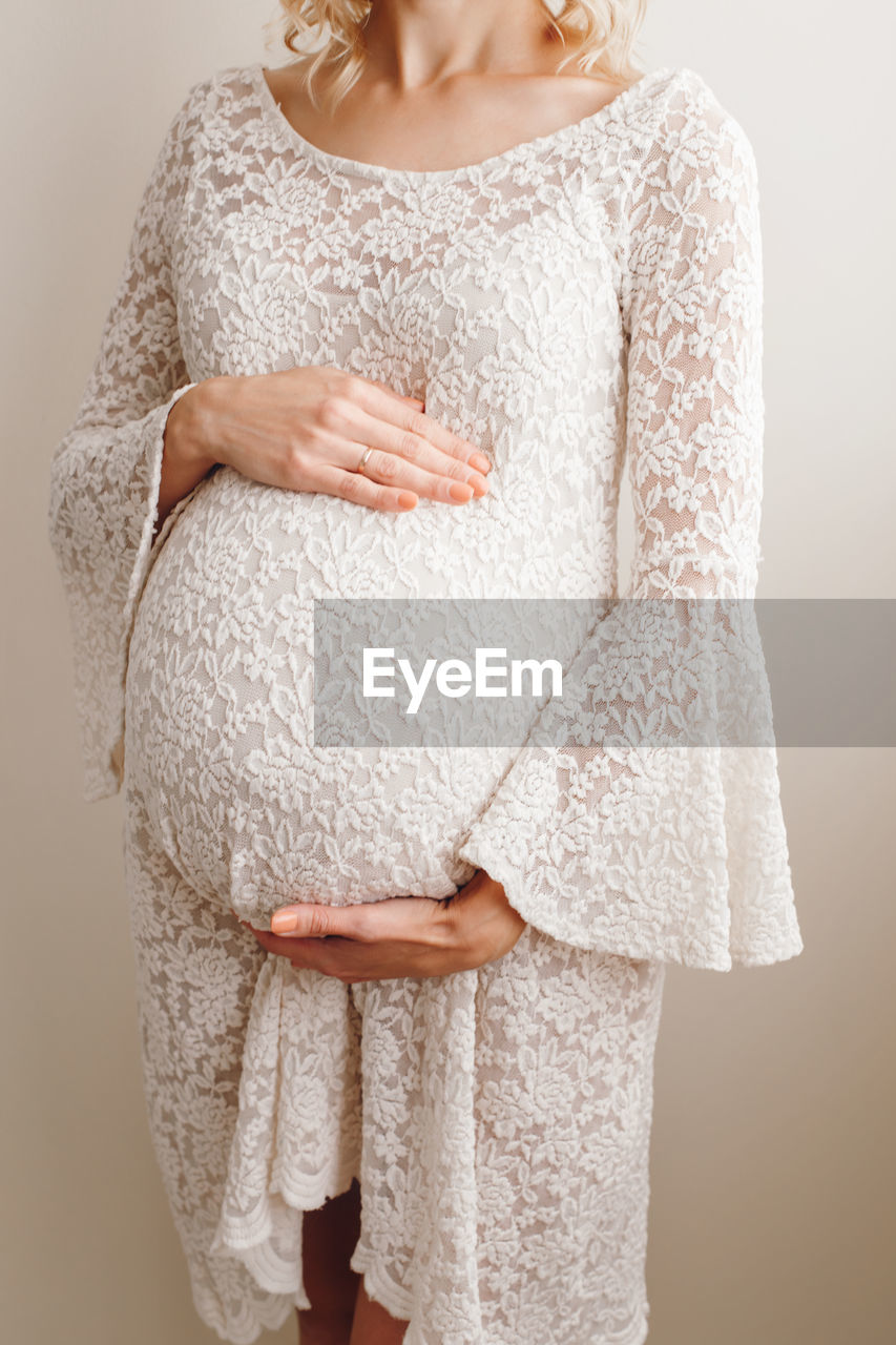 Midsection of pregnant woman standing against wall