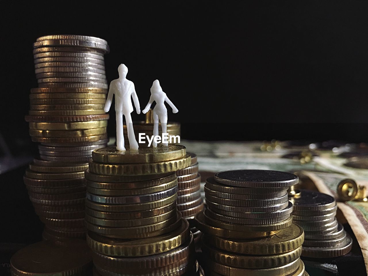 Figurines on stack of coins against black background