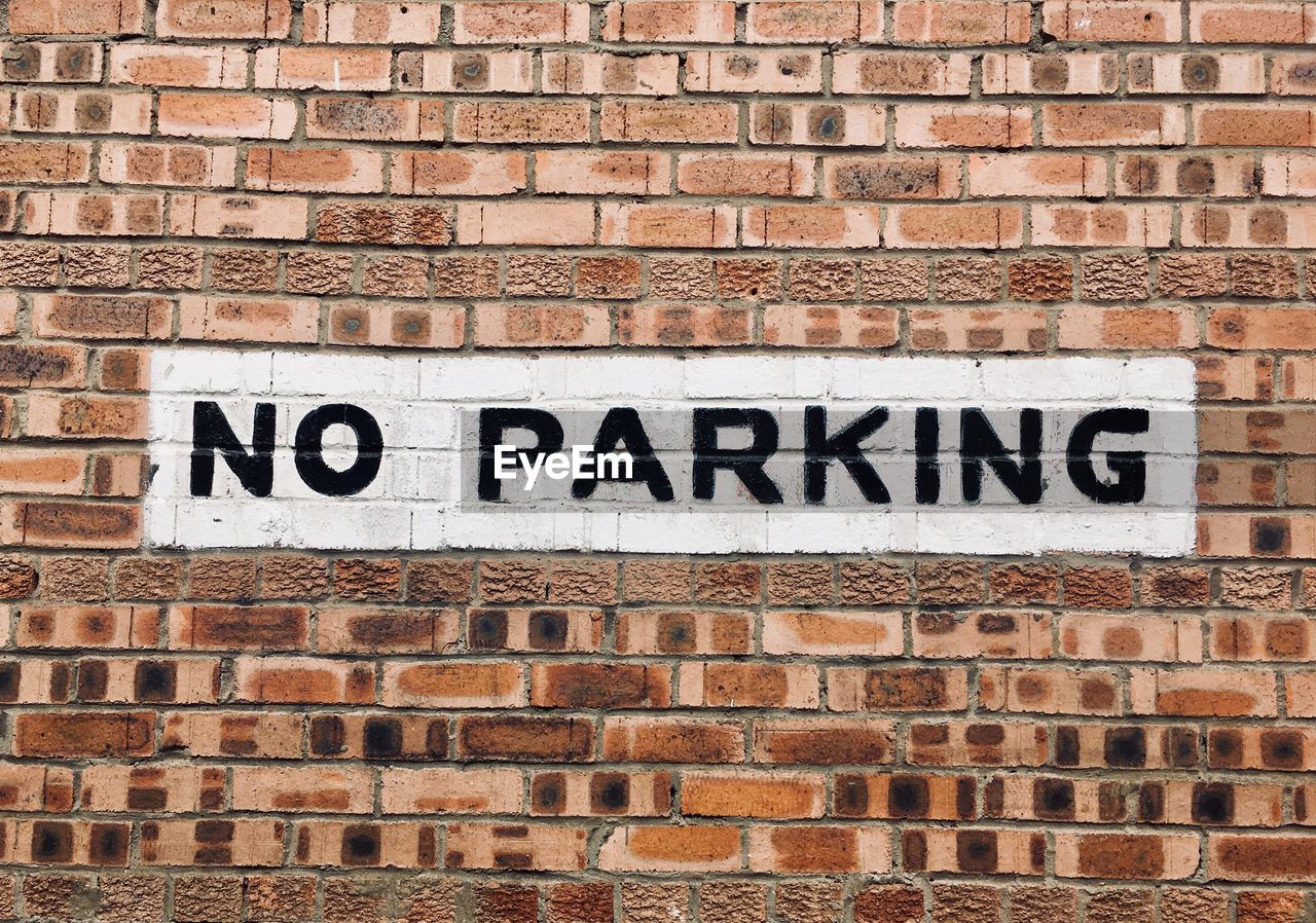 Close-up of no parking sign on brick wall