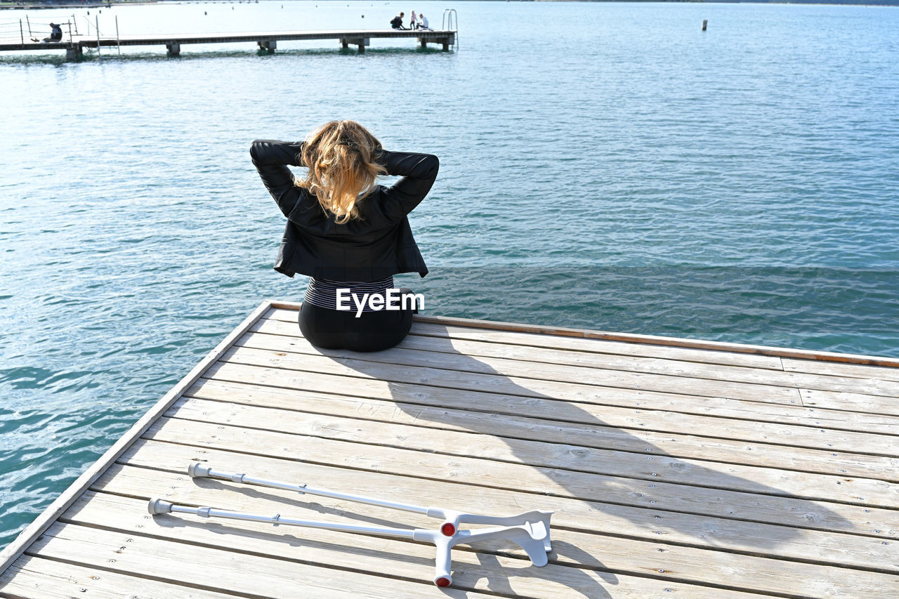 Rear view of man sitting on pier over sea