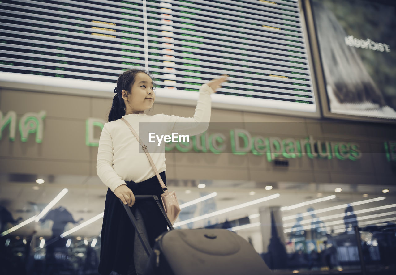 Low angle view of girl with luggage standing in airport