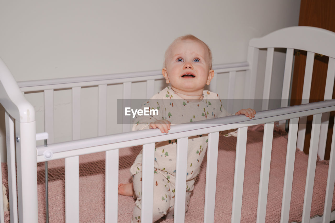 infant bed, baby, crib, child, nursery, childhood, bed, one person, cute, indoors, railing, room, innocence, portrait, furniture, babyhood, beginnings, person, baby clothing, clothing, emotion, white, lifestyles, staircase, looking at camera