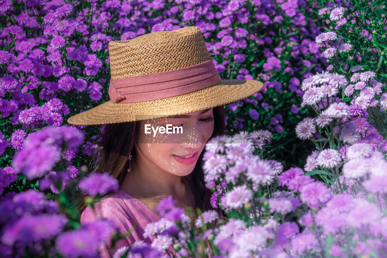 Close-up of woman wearing hat standing amidst flowering plants