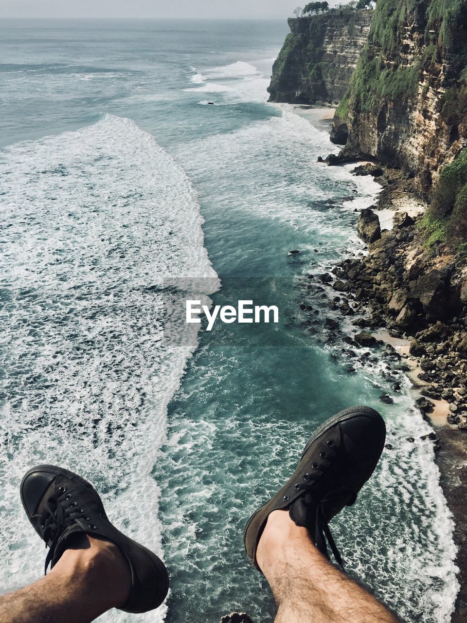 Low section of man relaxing on rock over sea against sky