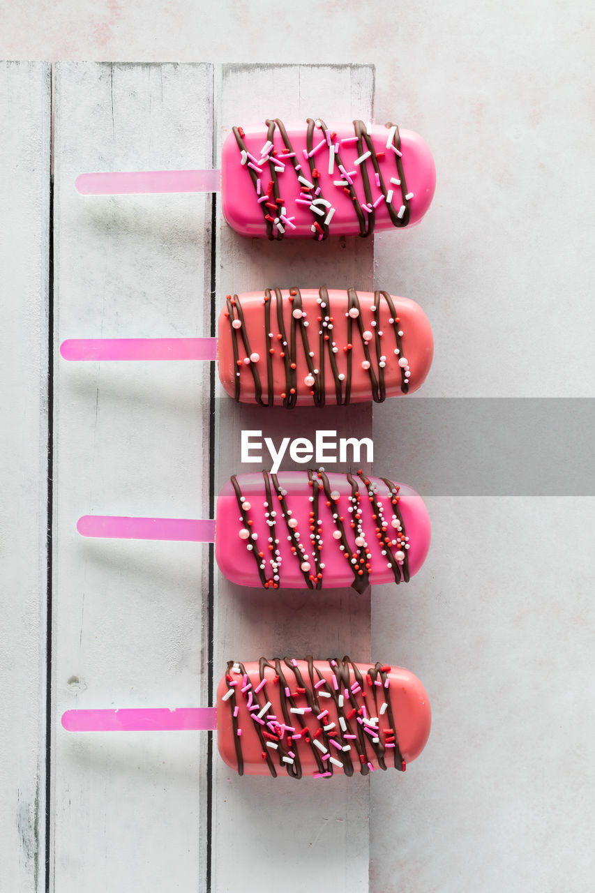 A row of decorated cakesicles for valentine's day, on a white wooden board.