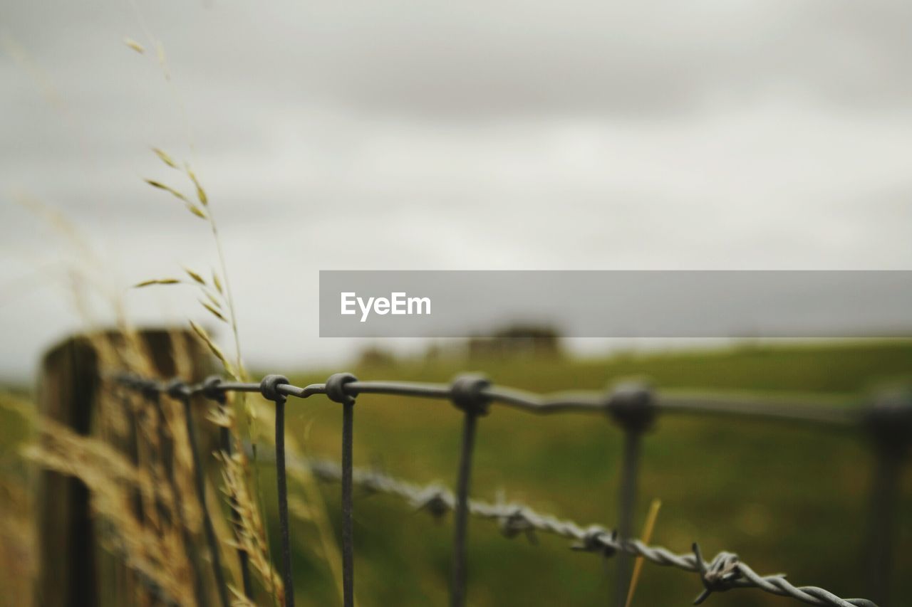 Close-up of barbed wire fence on field against sky