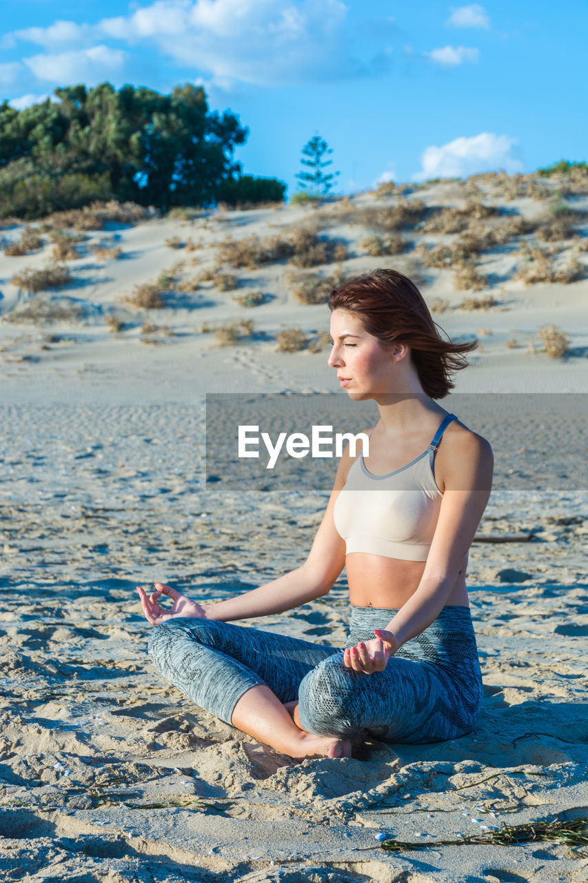 Young woman doing yoga at beach against sky