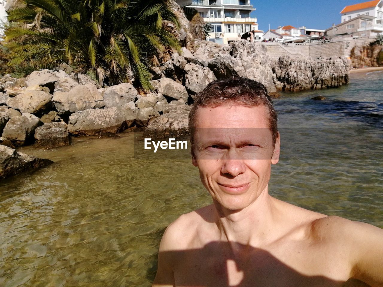 Shirtless man standing against river during sunny day