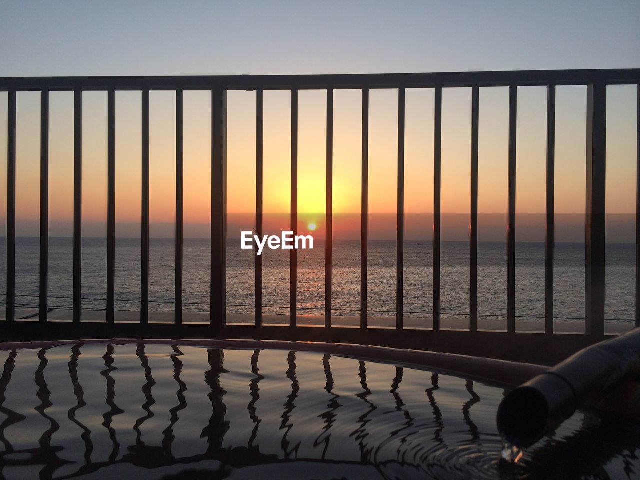 Railing over sea against sky during sunset