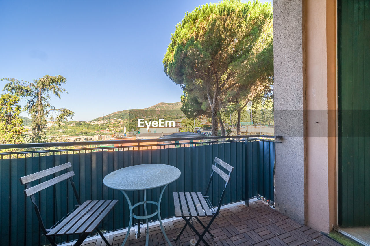 Empty chairs and table on balcony against sky and trees