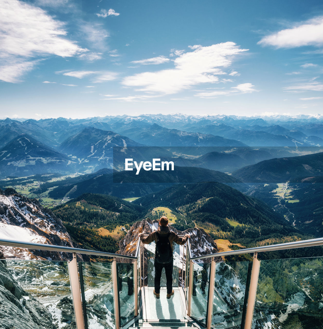 Man standing on footbridge over mountains against sky