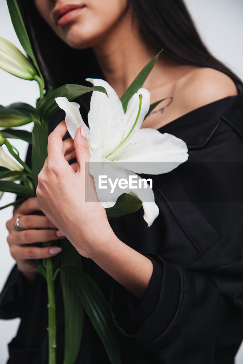 MIDSECTION OF WOMAN HOLDING FLOWER STANDING BY POTTED PLANT