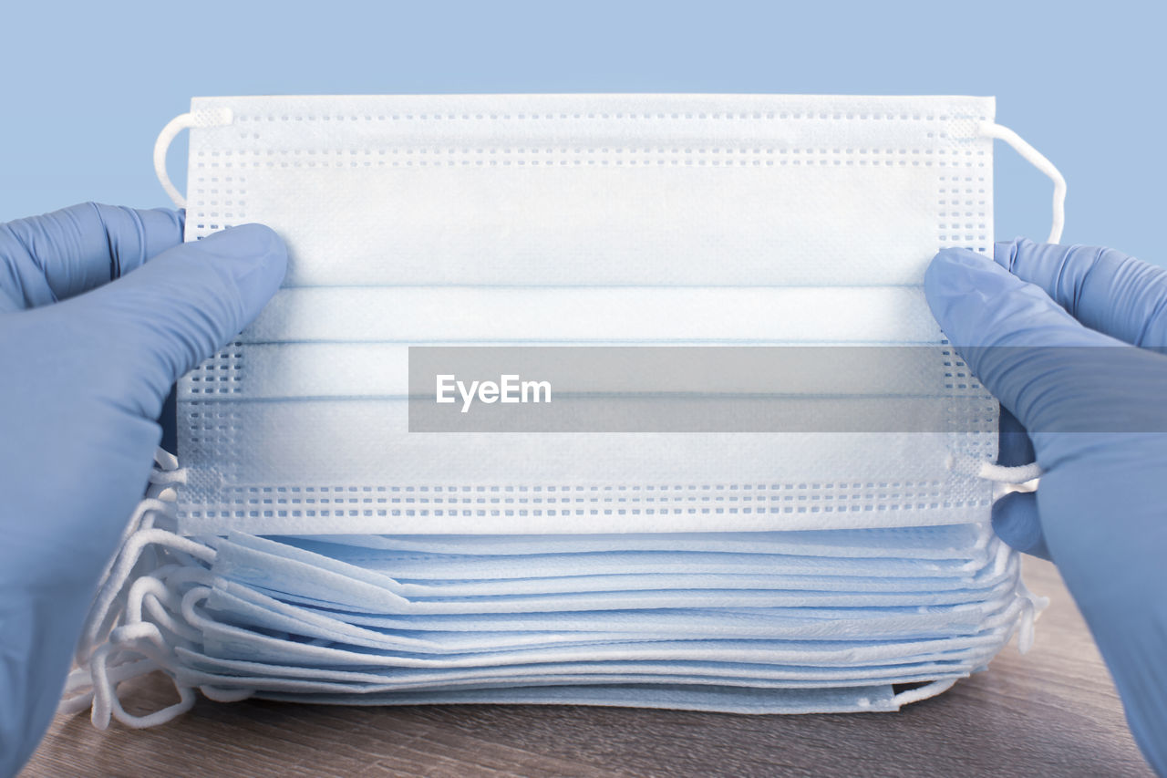 Medical personnel hand holding medical disposable face mask on wooden table