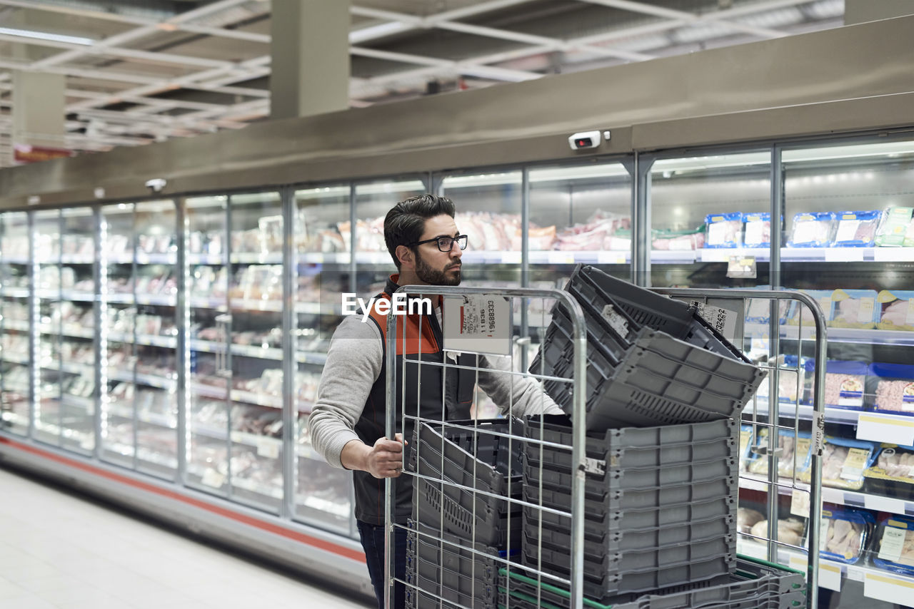 Sales clerk pushing cart with plastic crates at supermarket