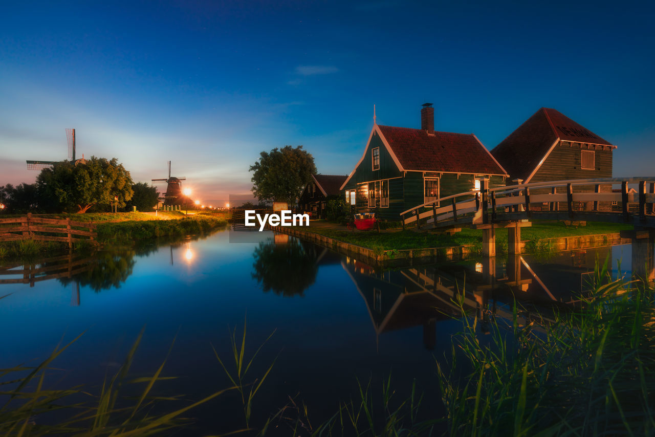 SCENIC VIEW OF LAKE BY ILLUMINATED BUILDINGS AGAINST SKY