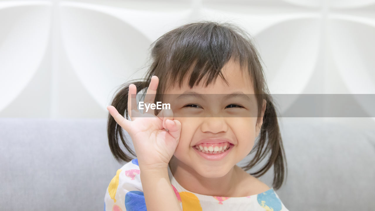 Charming 4 year old cute baby asian girl, little child with pigtails hair smiling showing ok finger.