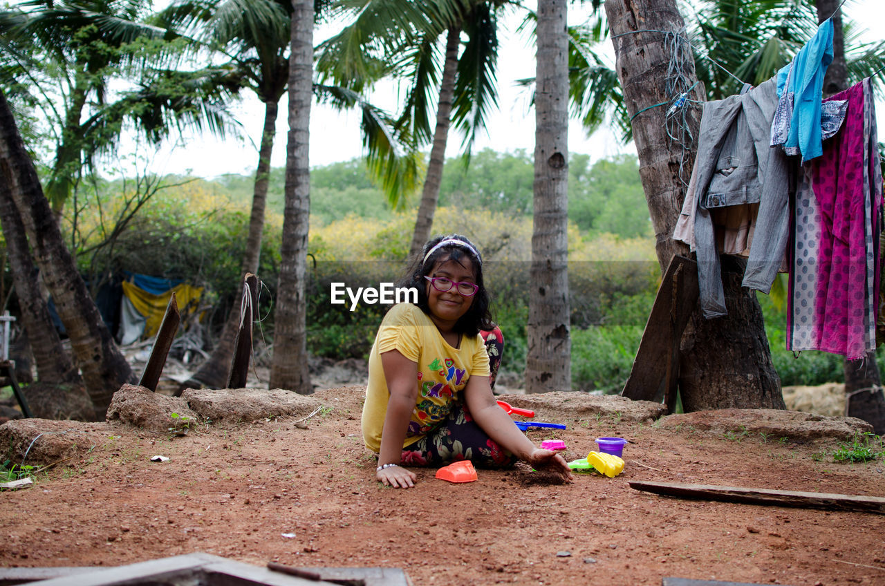 Portrait of smiling girl with toys sitting against palm trees