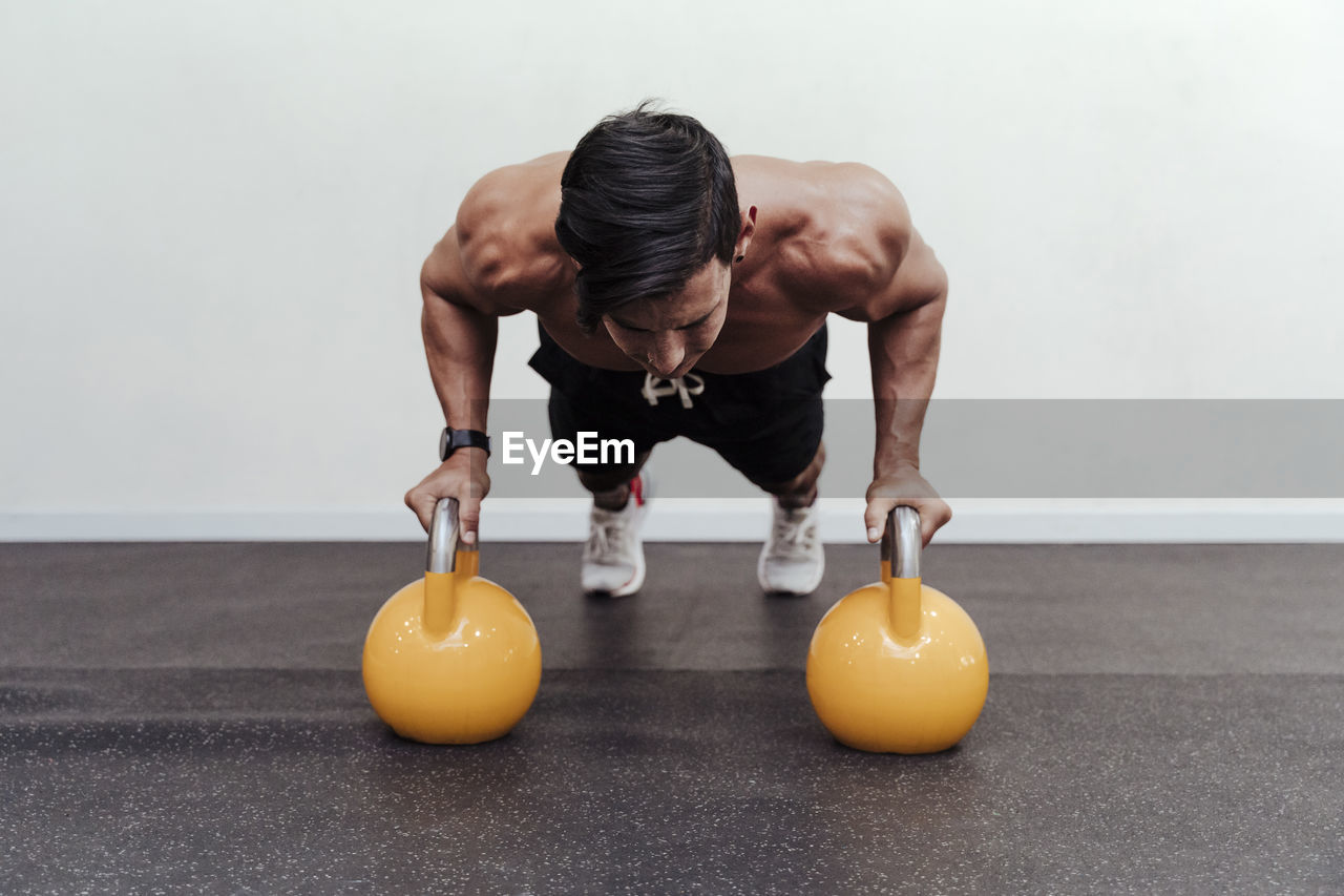 Male athlete doing push-ups on yellow kettlebell in gym