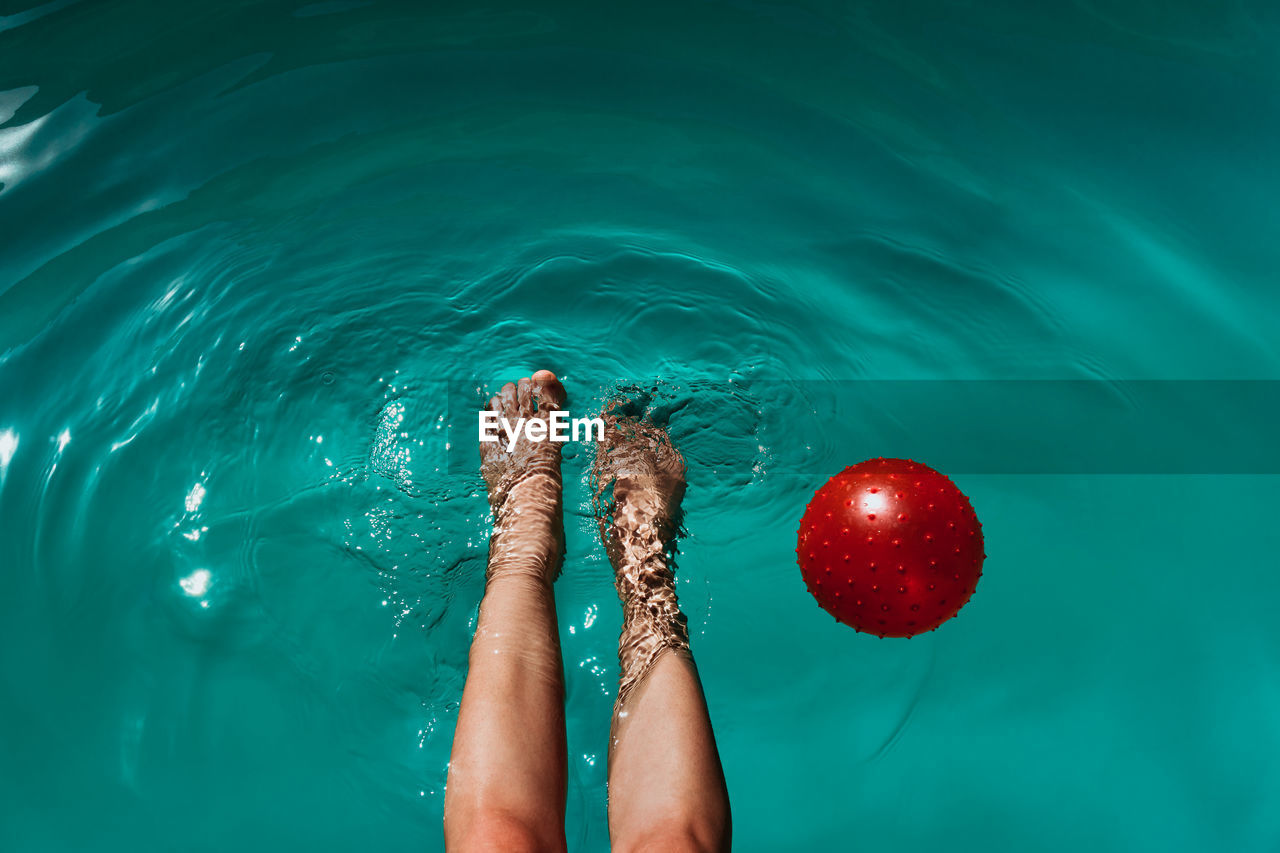 Low section of woman with ball swimming in pool