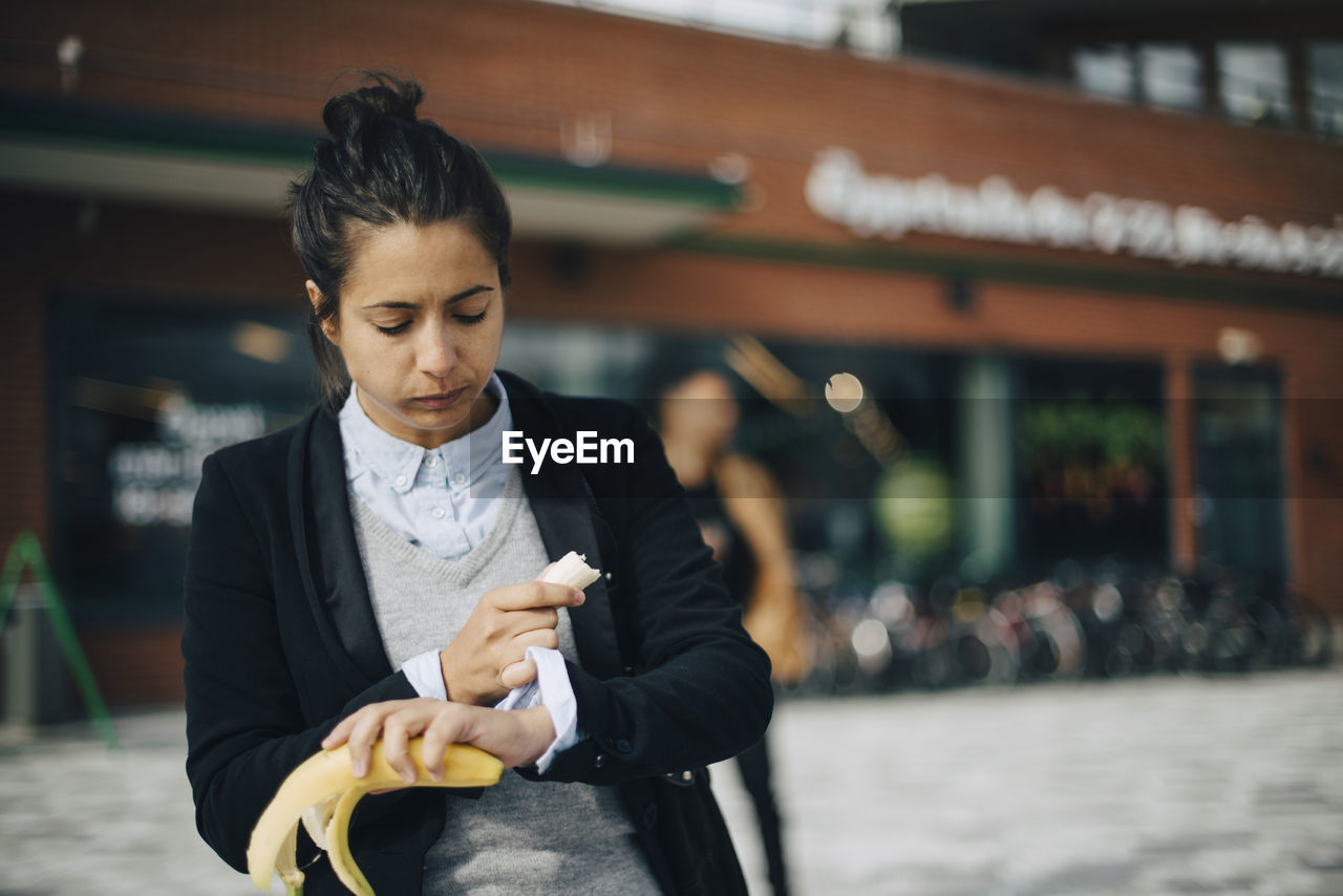 Woman checking time while eating banana at city