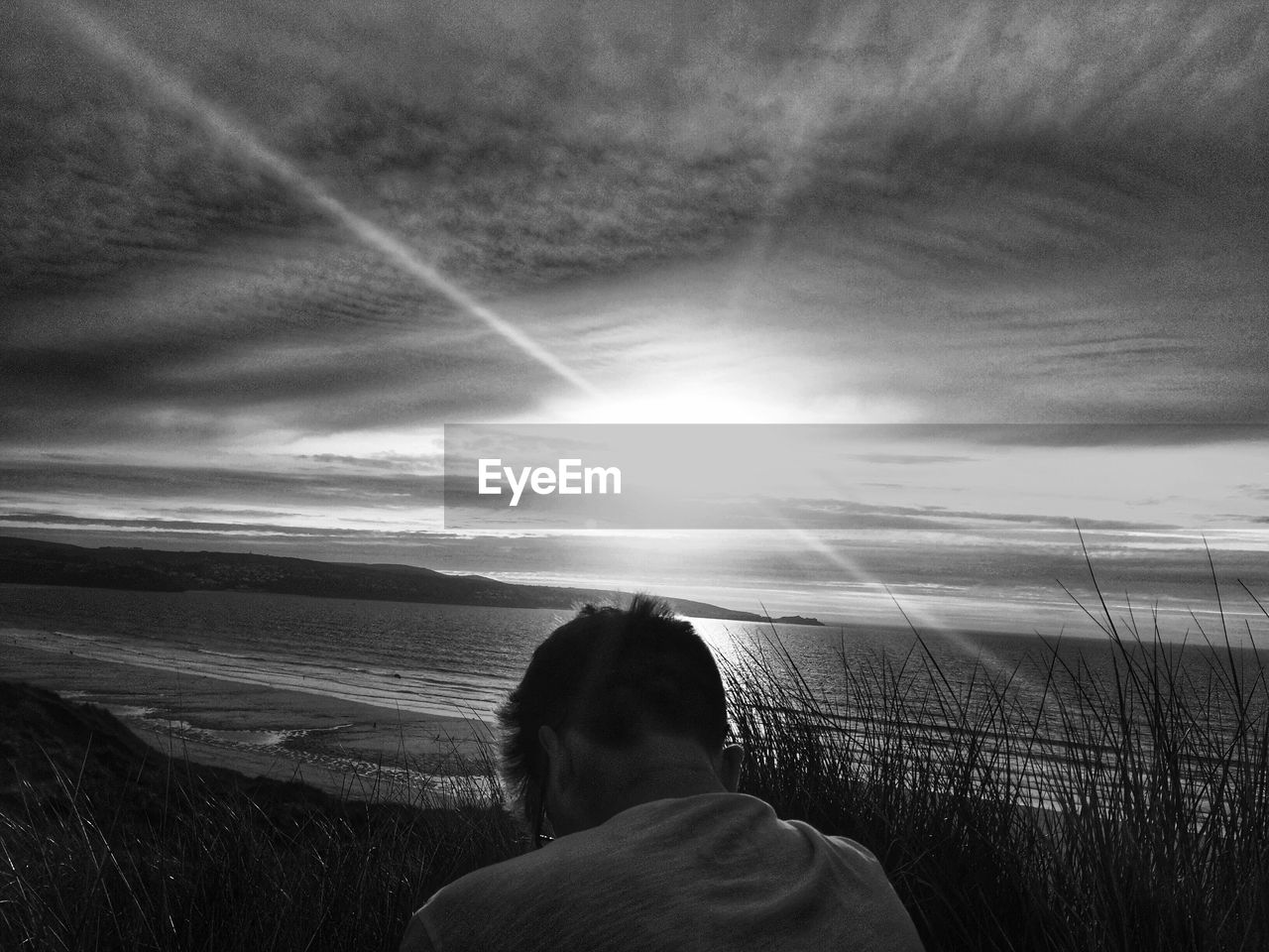 Rear view of man at beach against cloudy sky