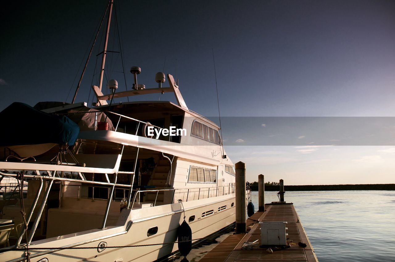 Yacht moored at harbor against blue sky during sunset