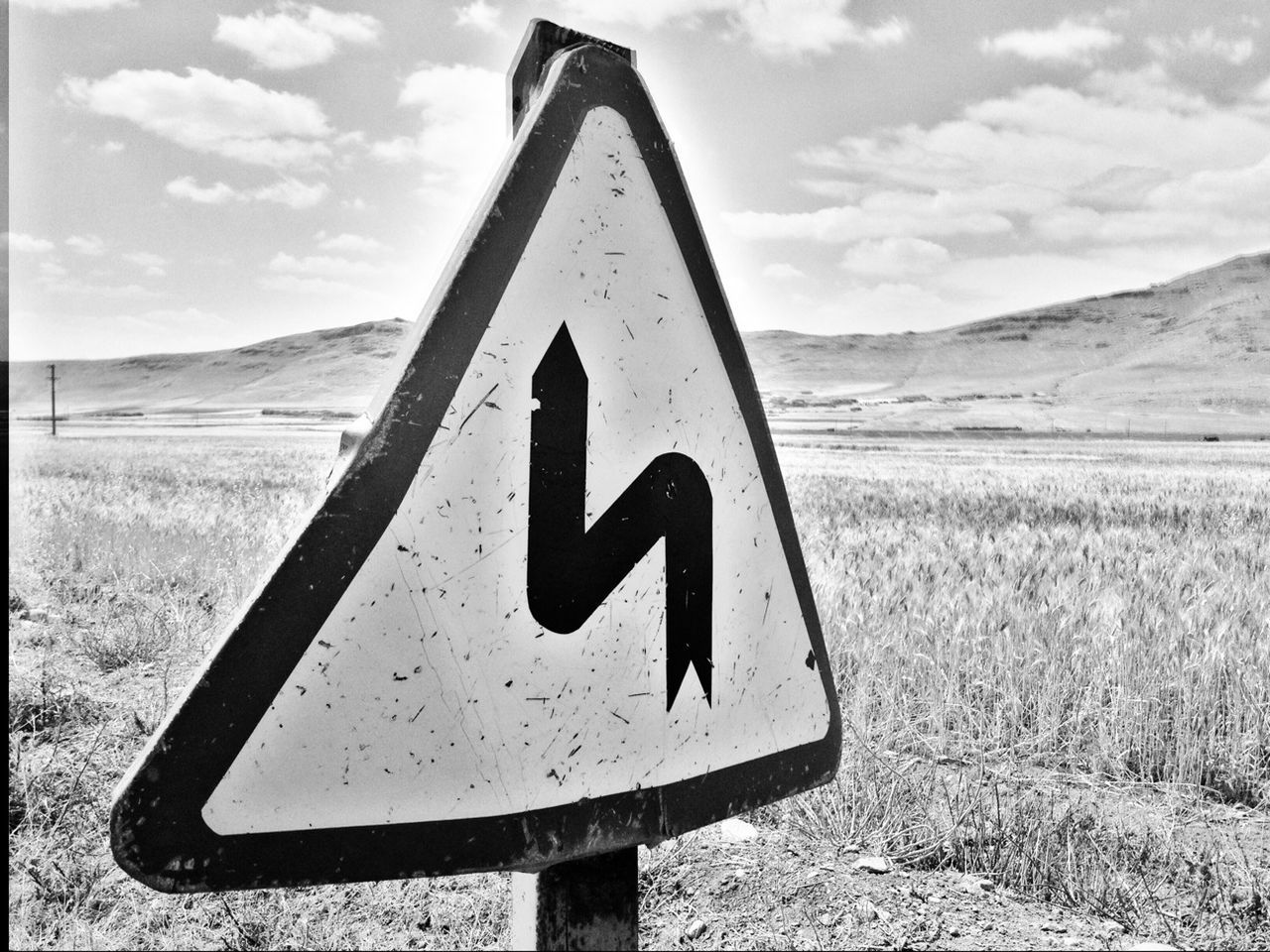 sign, black and white, communication, triangle shape, road, road sign, monochrome photography, sky, warning sign, nature, no people, guidance, cloud, traffic sign, triangle, monochrome, landscape, shape, environment, land, information sign, symbol, day, outdoors, white, signage, transportation