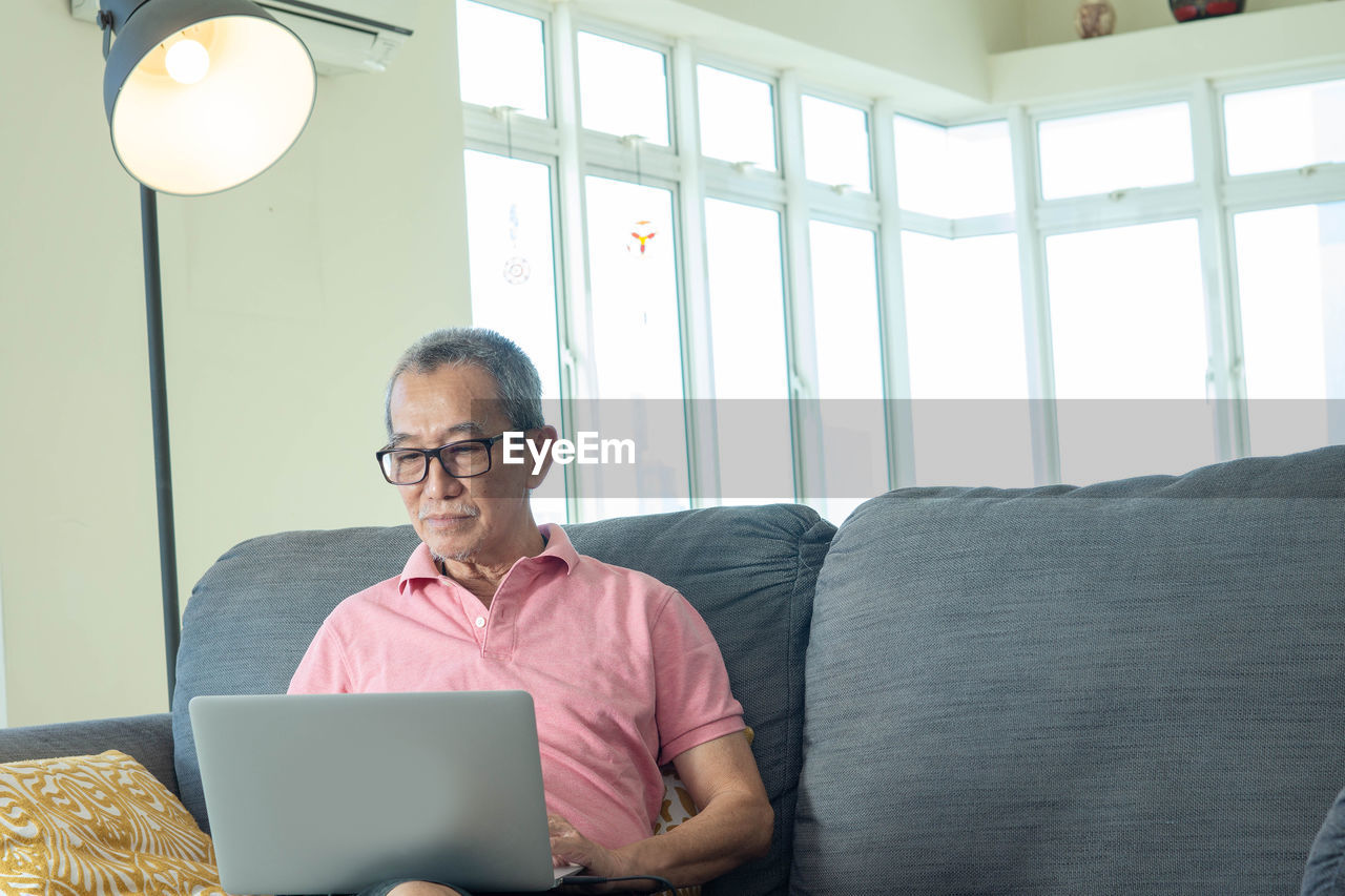 FULL LENGTH OF MAN SITTING ON SOFA AT HOME