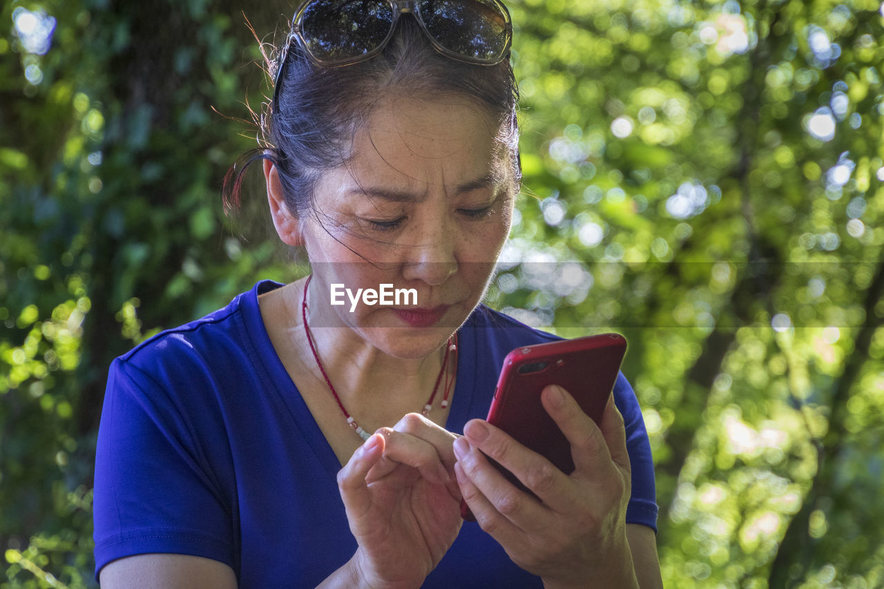 Close-up of senior woman using smart phone against trees in forest