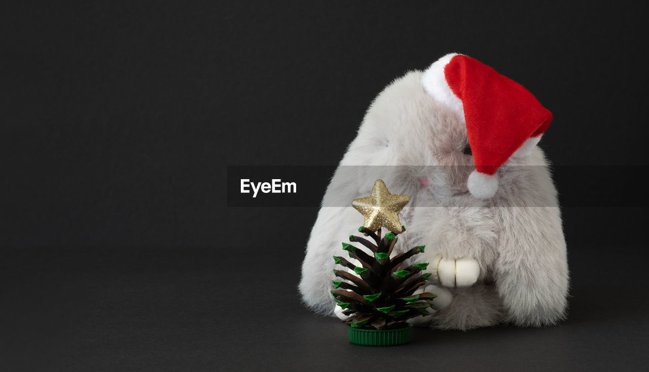 Toy gray bunny in santa hat with christmas tree made of pine cone with space for your text