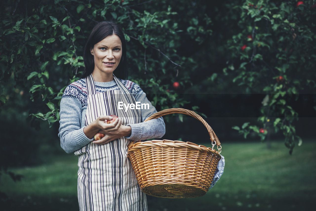 Portrait of woman carrying wicker basket at apple orchard