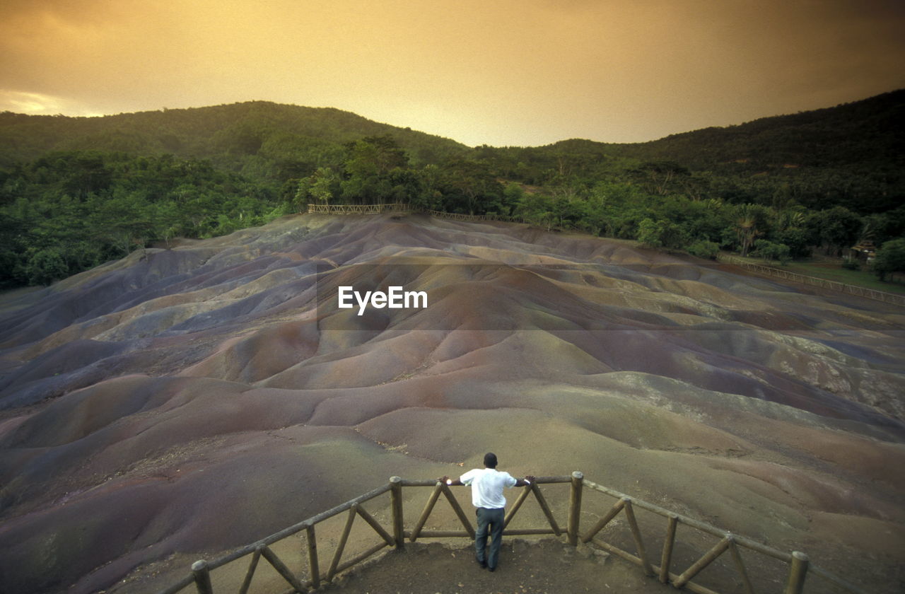 Rear view of man standing on lookout tower looking at mountain ranges during sunset