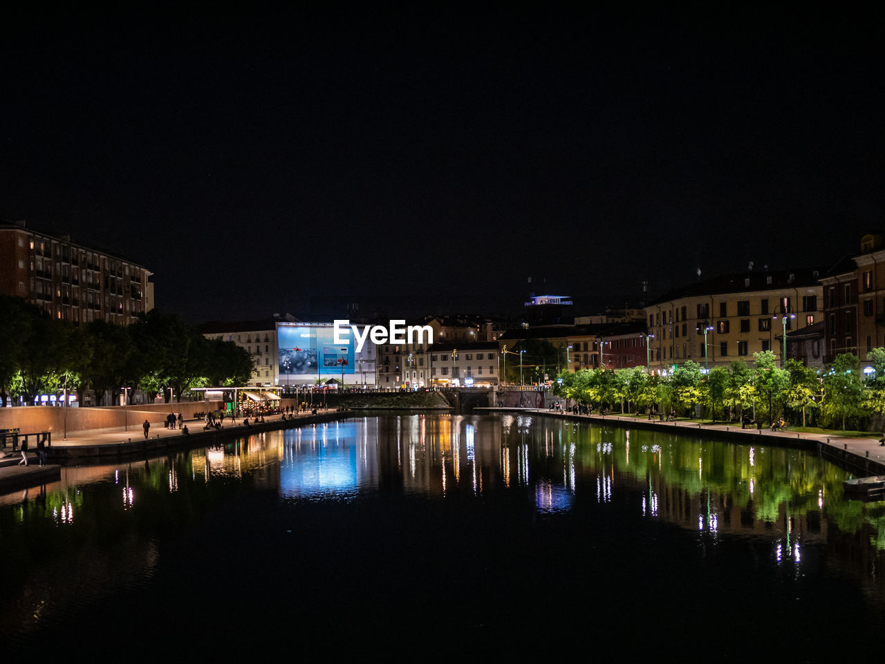 ILLUMINATED BUILDINGS BY RIVER AGAINST SKY