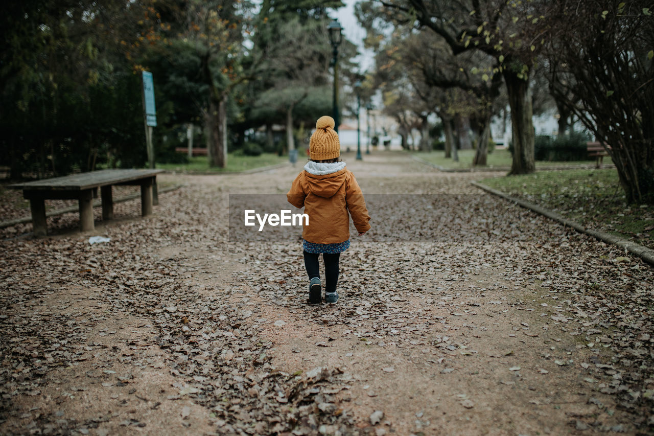 Rear view of girl walking on footpath in park during winter