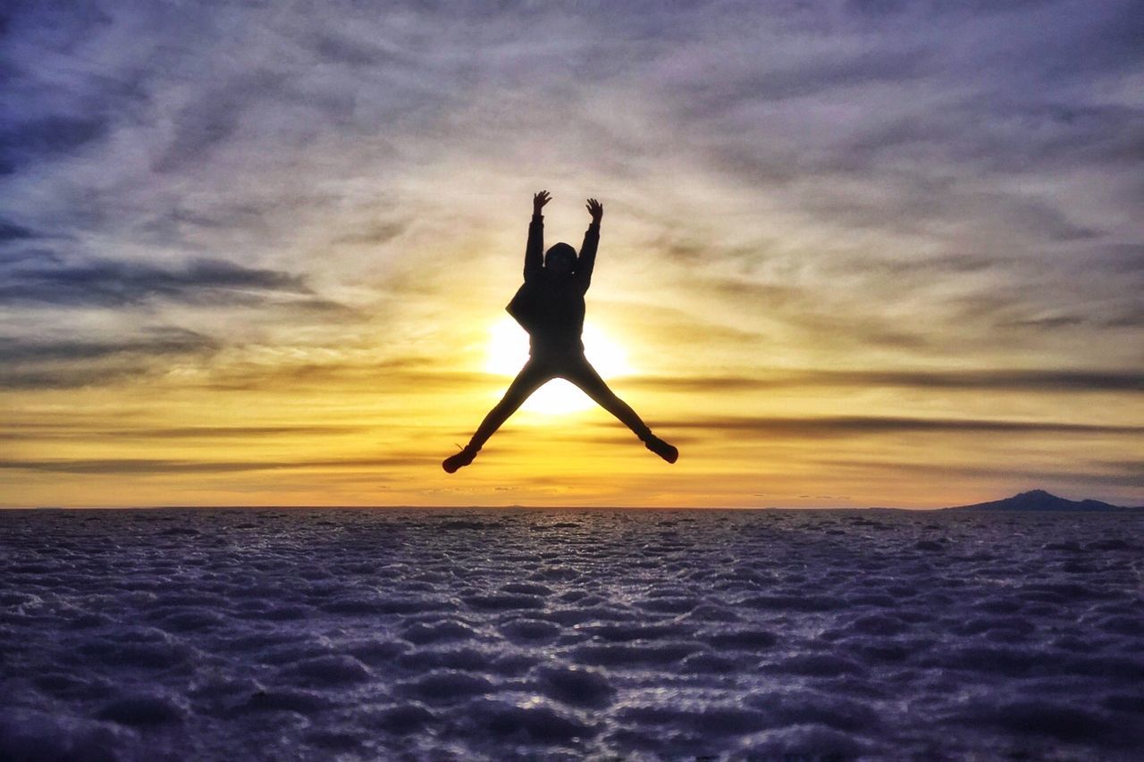 Silhouette woman jumping over sea against sky during sunset