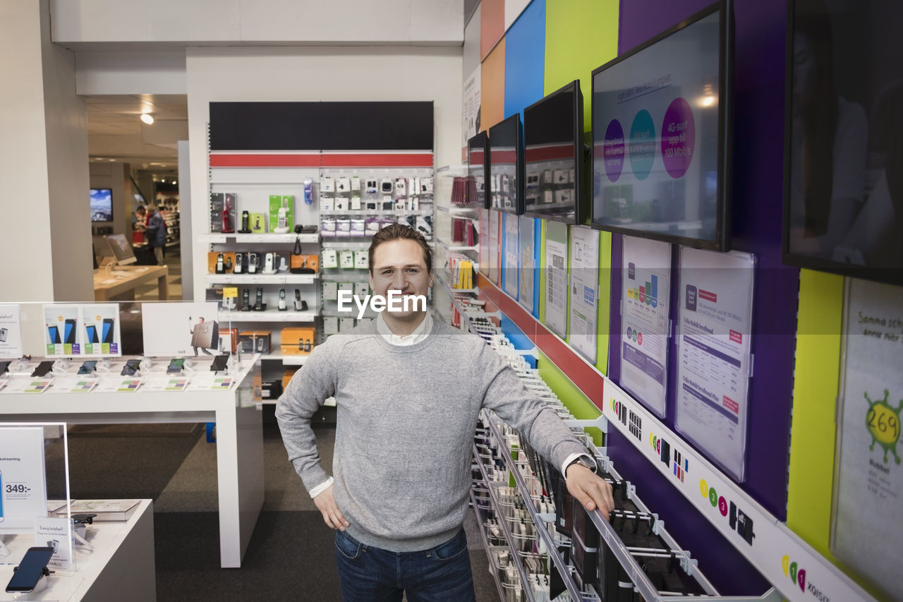 Portrait of cheerful salesman standing in electronics store