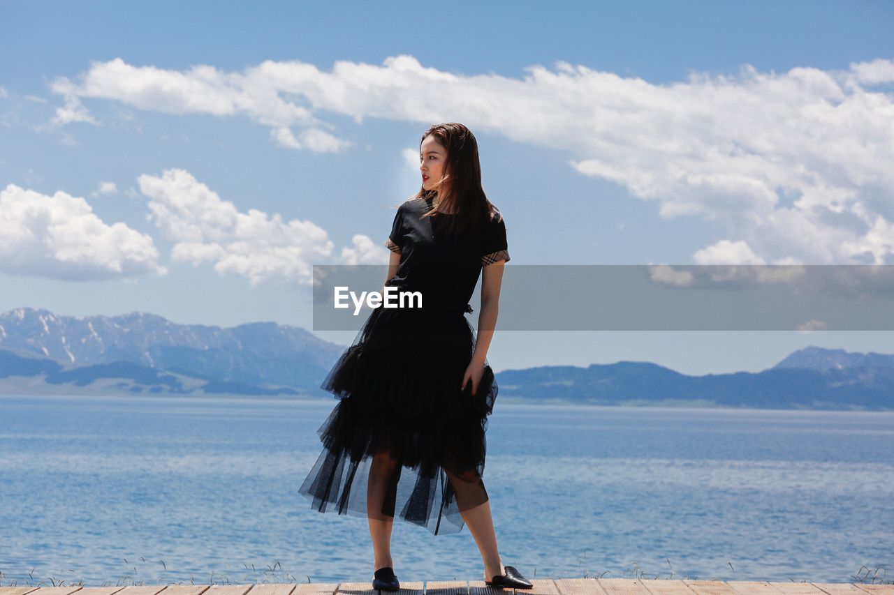 WOMAN STANDING AT SEA AGAINST SKY