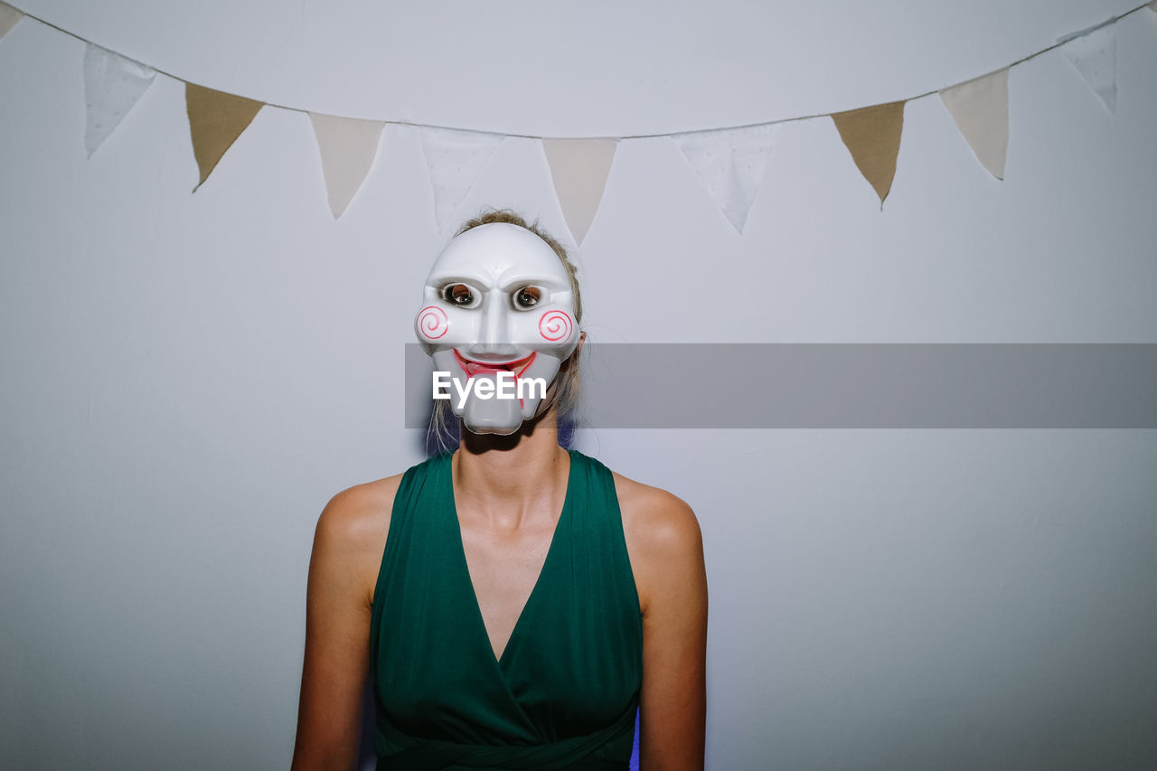 Portrait of woman wearing mask standing against wall