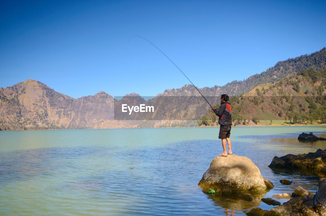 Man fishing standing on rock by lake