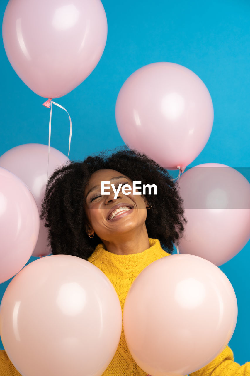 Happy pleased african woman holding a lot of pink balloons, enjoys cool party, celebrates birthday