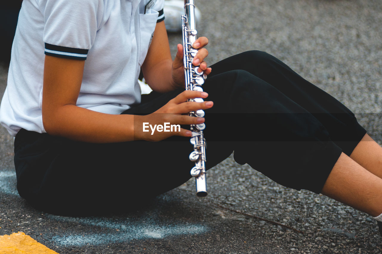 Midsection of woman playing flute while sitting on footpath