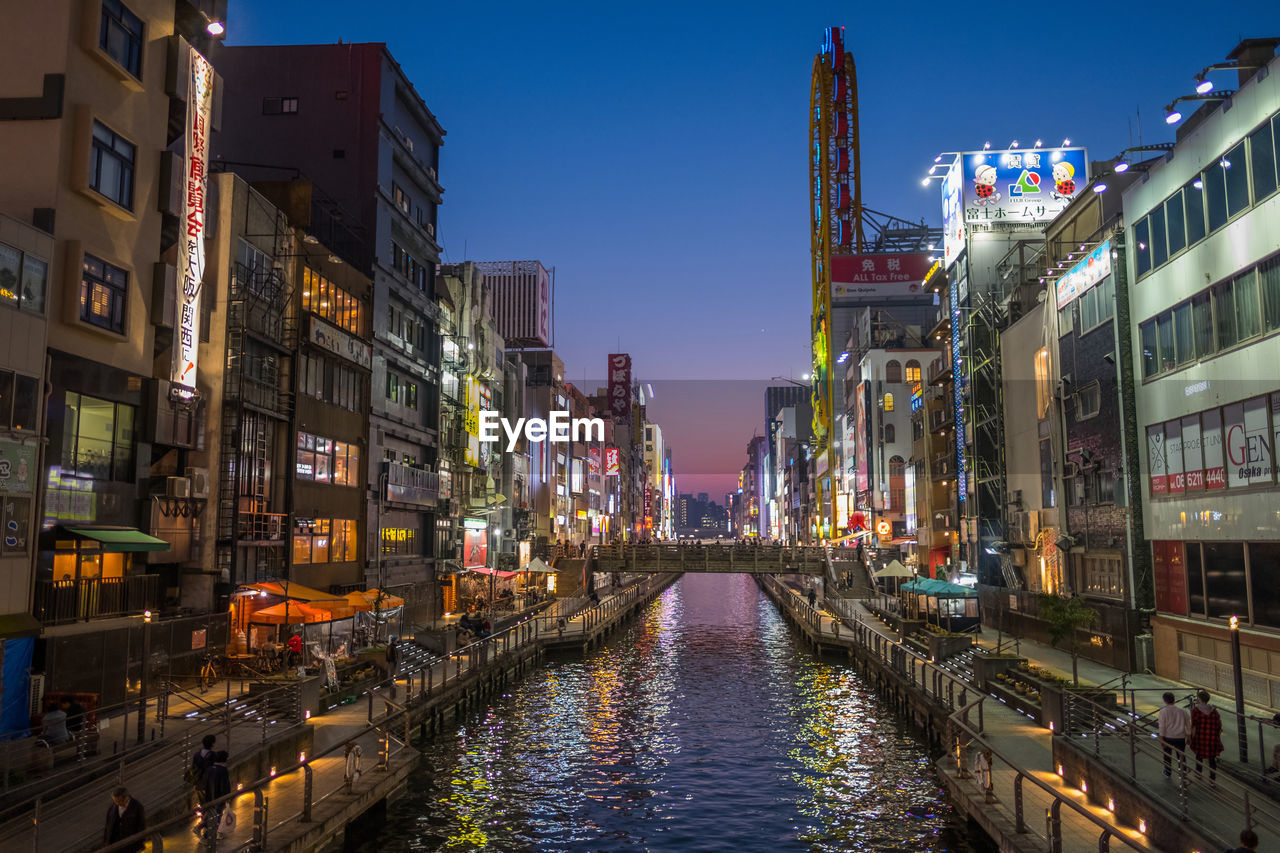 Canal amidst illuminated buildings in city during sunset