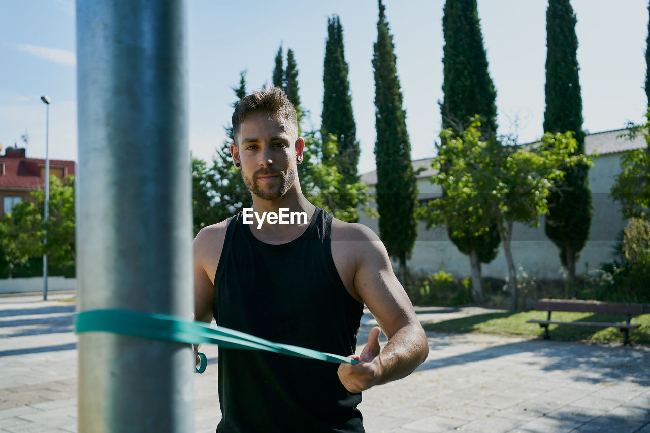 Young man practicing calisthenic with an elastic band in a park