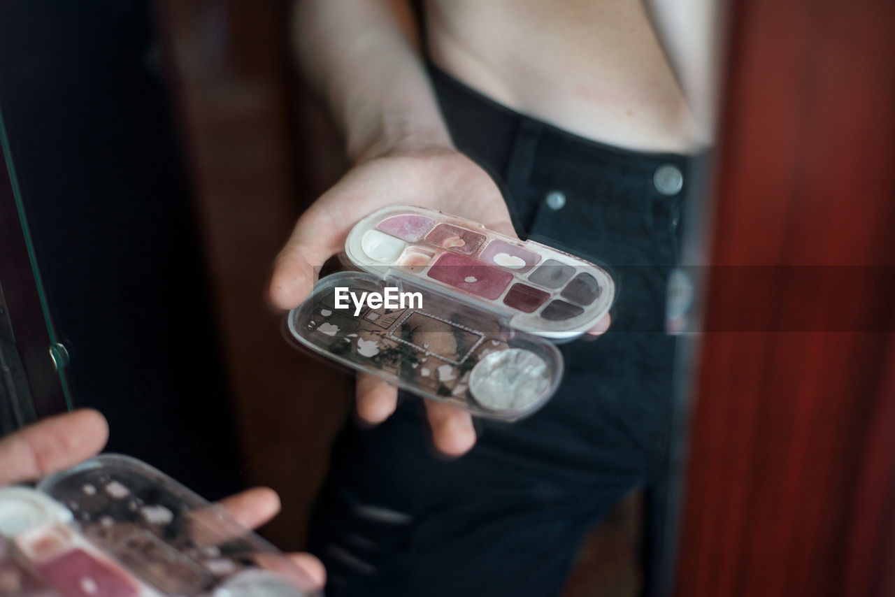 Reflection of man holding beauty product while standing in front of mirror