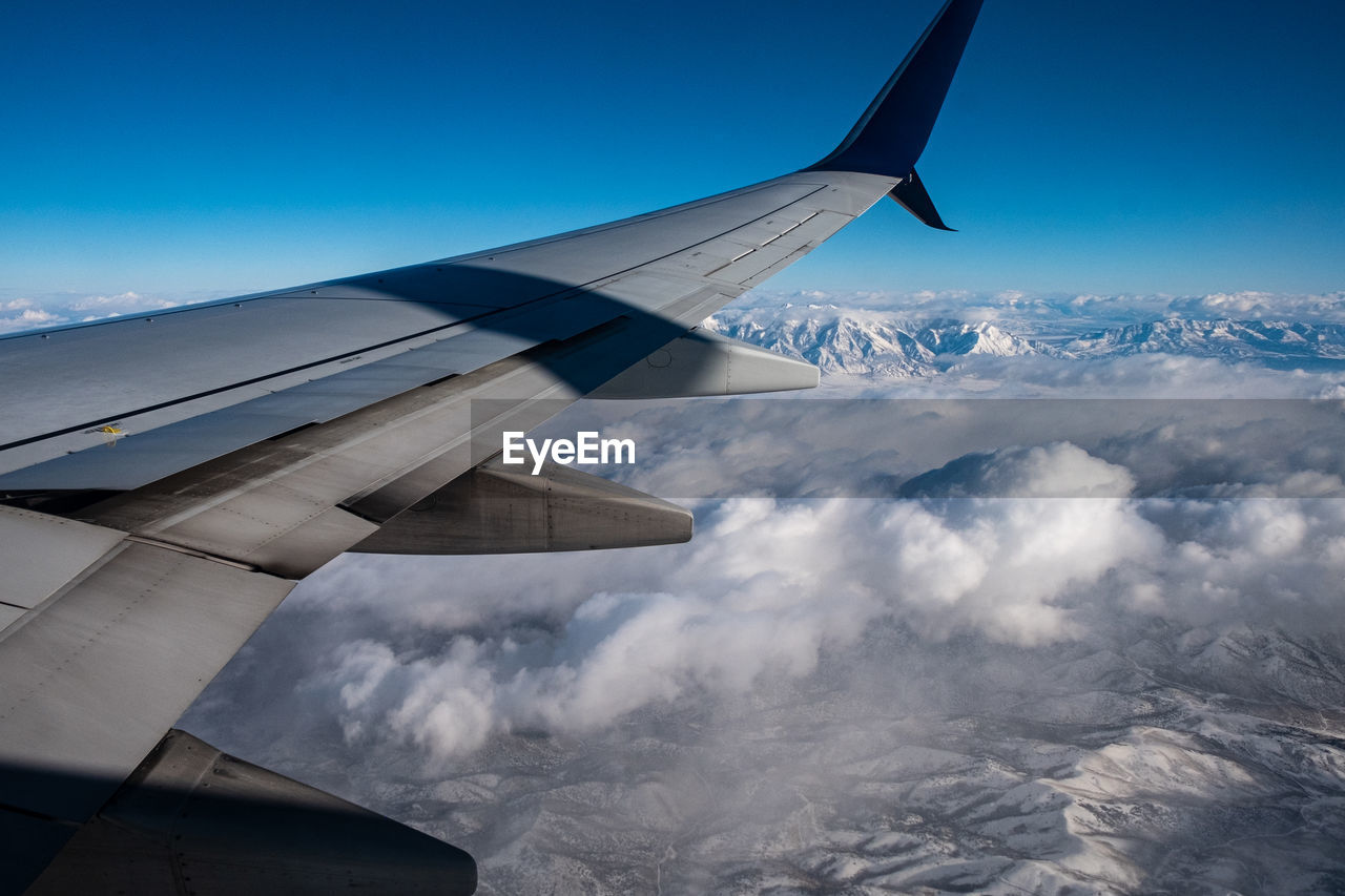 AIRPLANE FLYING OVER SNOWCAPPED MOUNTAIN AGAINST SKY