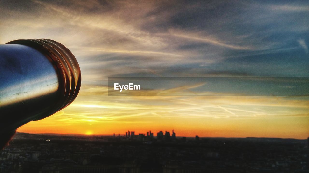 Coin-operated binoculars against cityscape at sunset