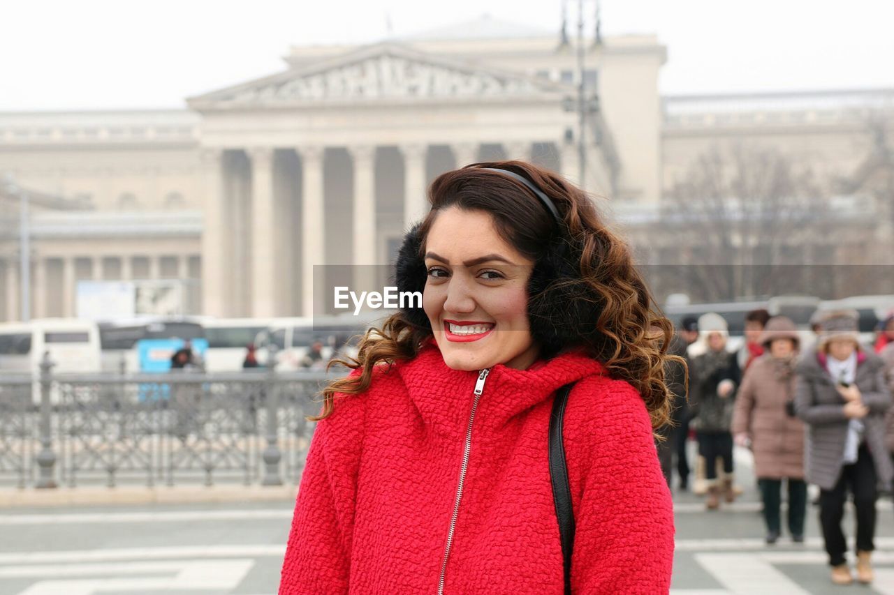 Portrait of smiling young woman standing on city street in foggy weather